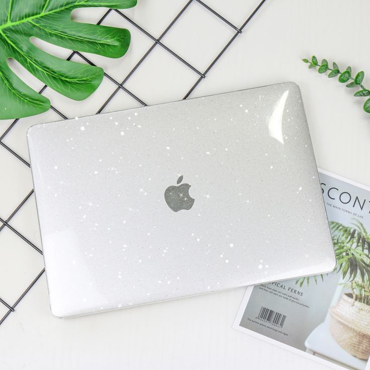 an apple laptop computer sitting on top of a table next to a plant and magazine