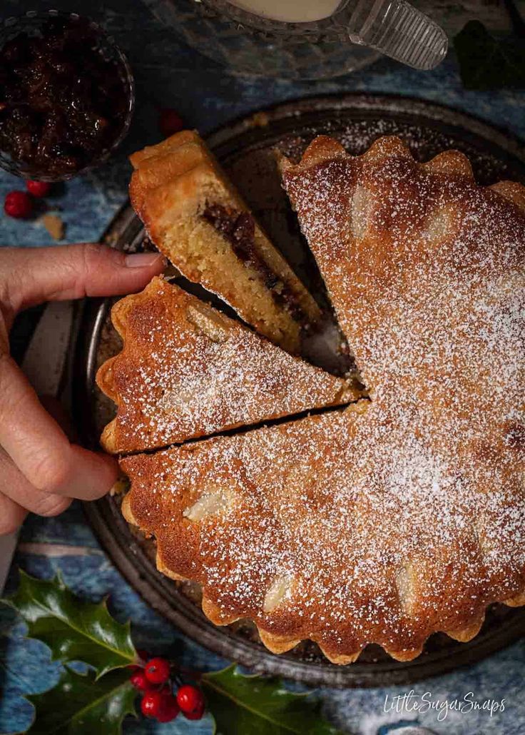 a person is cutting into a cake with powdered sugar on top and holly decorations around the edges