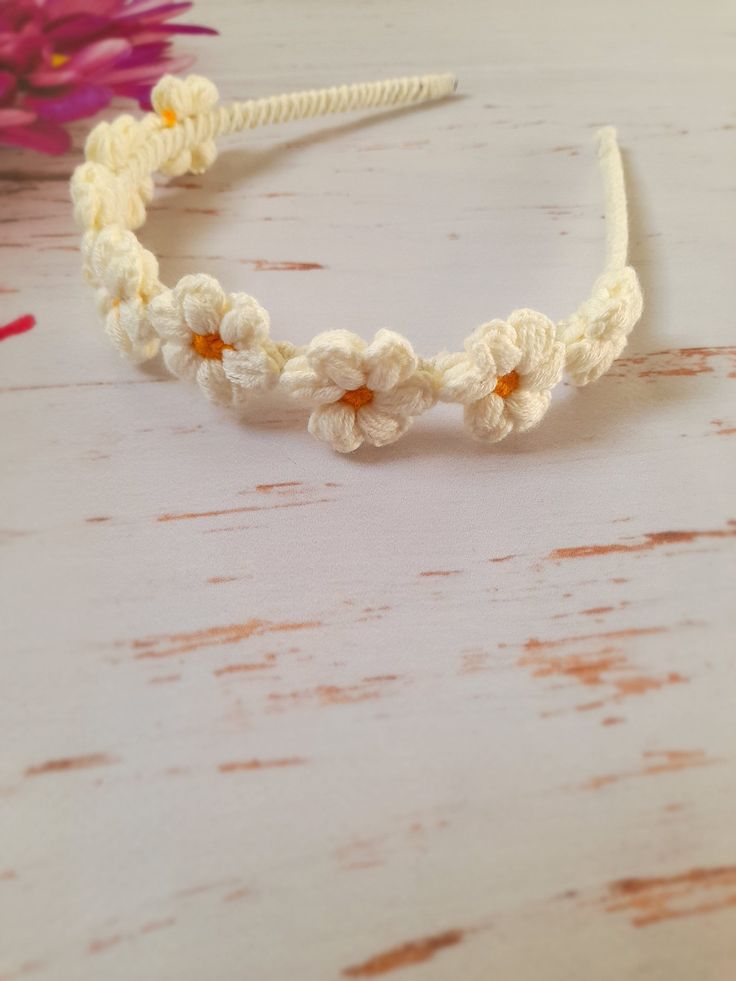 a crocheted headband with flowers on it sitting on a table next to pink flowers