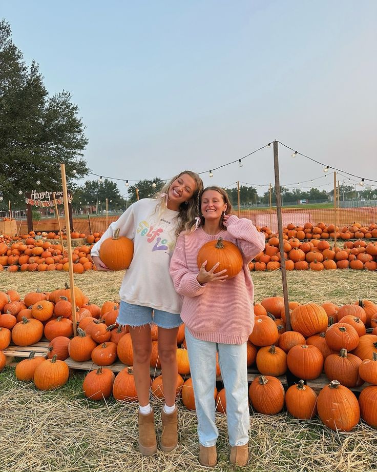 two girls standing next to each other holding pumpkins in front of rows of pumpkins