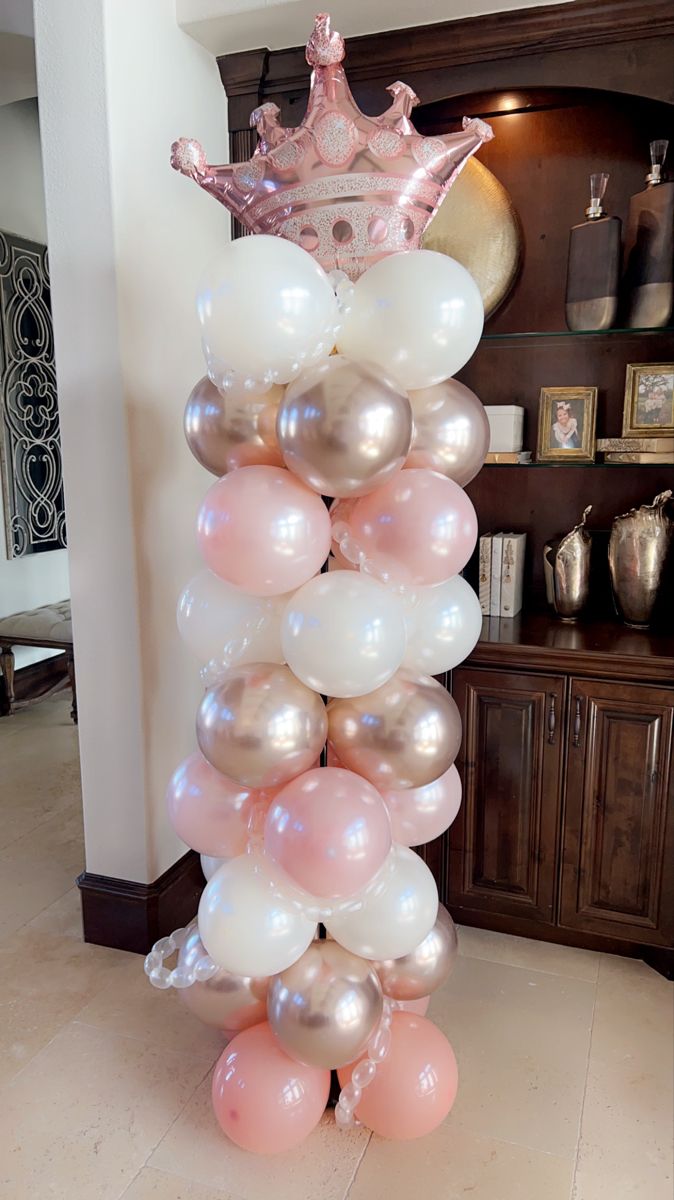 a tall balloon tower with balloons and a tiara on top is in the middle of a living room