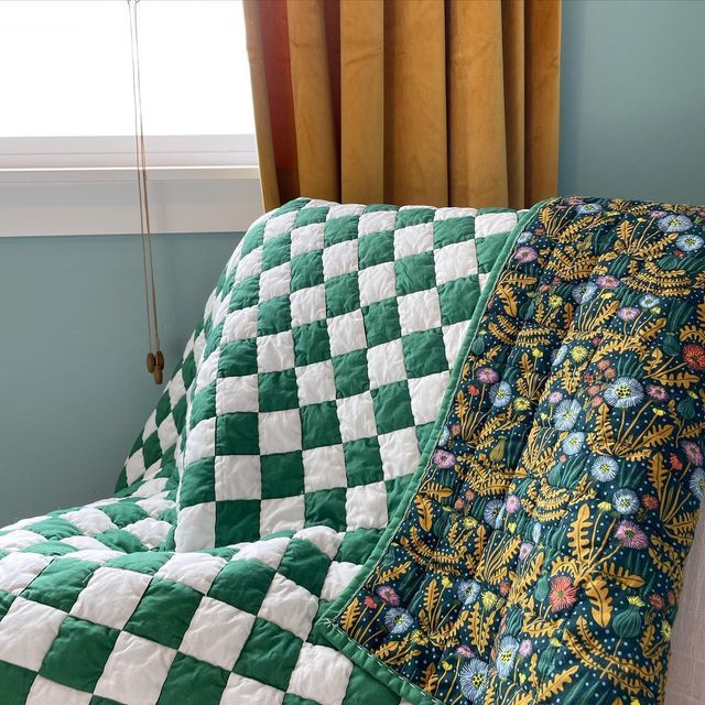 a green and white quilt sitting on top of a couch in front of a window