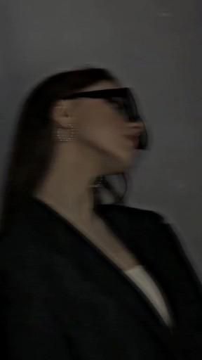 a blurry photo of a woman with her head tilted to the side wearing glasses