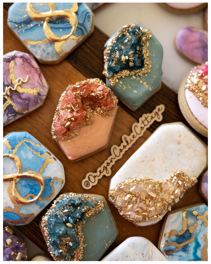 many decorated cookies on a table with gold and blue frosting in the shape of hearts