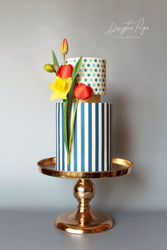 a three tiered cake decorated with flowers and polka dots on a gold plated stand