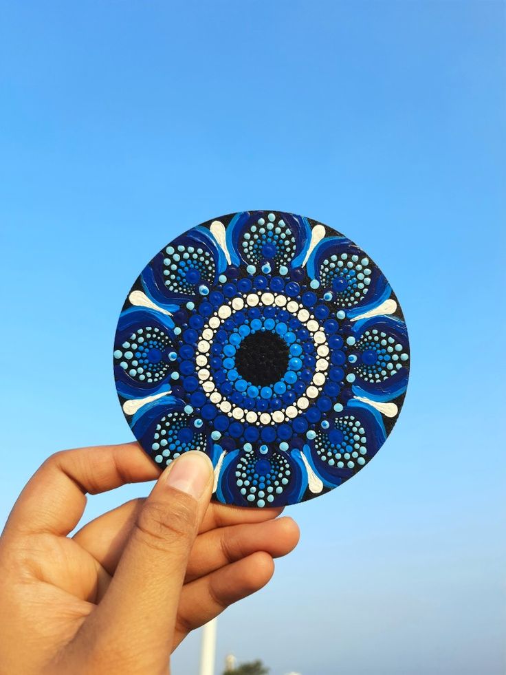 a hand holding up a blue and white circular object in front of a blue sky