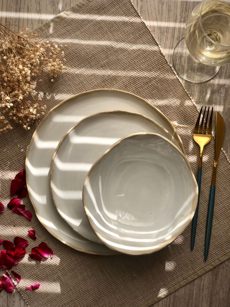 three white plates with gold rims are sitting on a placemat next to two forks and a glass of wine