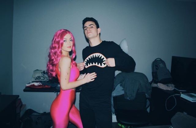 a man standing next to a woman in a pink bodysuit with a shark mouth on it