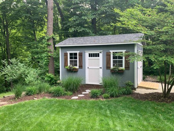 a small shed in the middle of some trees and grass with windows on each side