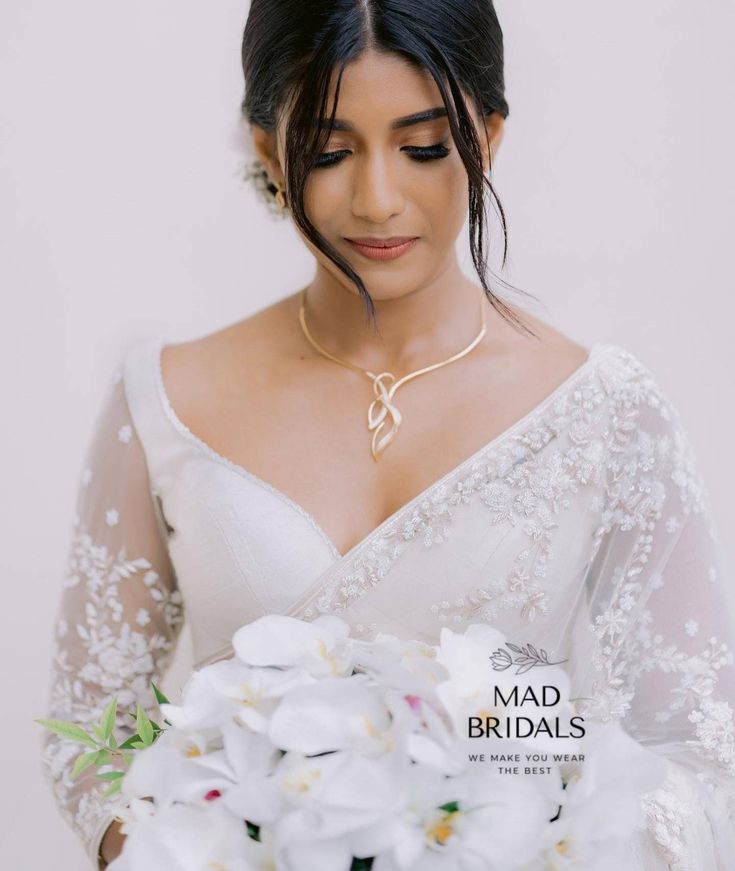 a woman in a white dress holding a bouquet of flowers and wearing a gold necklace