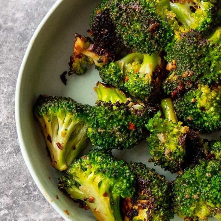 broccoli florets in a white bowl on a gray table top with some seasoning sprinkles