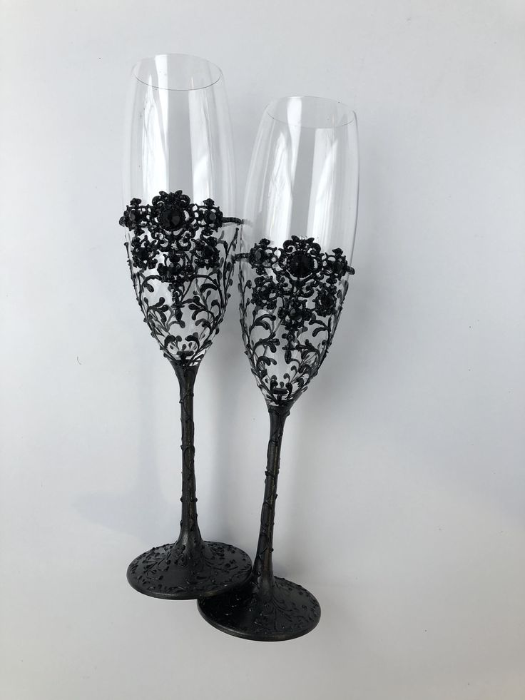 two wine glasses sitting next to each other on top of a white surface with black flowers