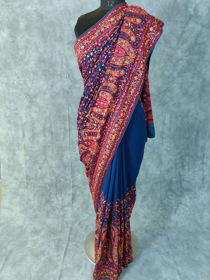 Kashmiri Embroidered Saree on Georgette with thread embroidery and some stones Fabric: Georgette Length: 5.5 Meters | 6.1 yards Colour: Dark Teal Blue Blouse: Saree comes with blouse fabric. Base Color is same as Saree with border for sleeves or however you desire Please see product video for product details. If you have any questions message us anytime. Fall and Edging will be done complimentary. Blouse Stitching (If Requested): Blouse will be stitched according to your measurements, which we w Bollywood Style Embroidered Pre-draped Saree For Diwali, Traditional Blue Pre-draped Saree With Resham Embroidery, Festive Jamawar Embroidered Fabric For Reception, Blue Bollywood Style Saree In Chinon, Bollywood Style Designer Embroidered Pre-draped Saree, Designer Bollywood Pre-draped Embroidered Saree, Blue Embroidered Pre-draped Saree For Transitional Season, Traditional Georgette Choli With Embroidered Border, Traditional Pre-draped Saree With Embroidered Border In Chinon