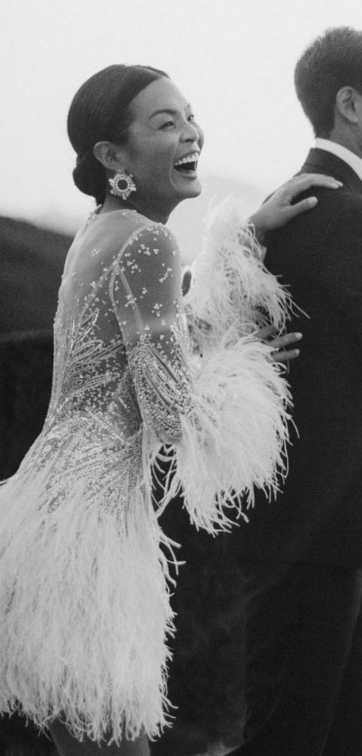 a black and white photo of a woman in a feathered dress standing next to a man