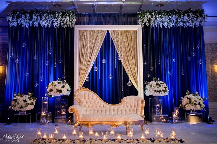 a couch sitting in front of a blue curtain with white flowers and candles on it