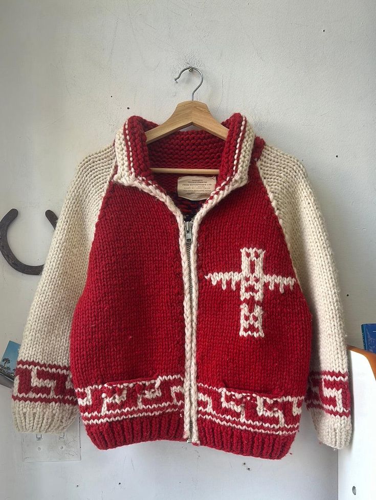 a red and white knitted jacket hanging up on a wooden hanger next to a wall