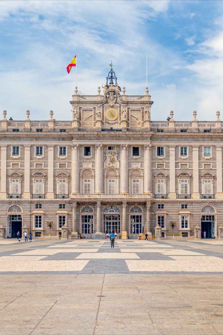 a large building with two flags on top of it's roof and people walking in front