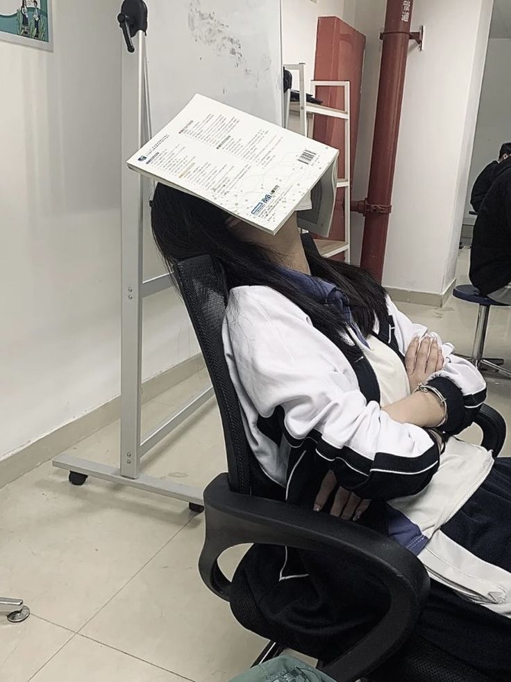 a woman sitting in a chair with a book on her head