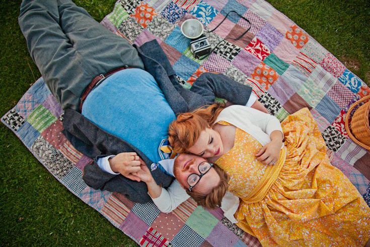 a man and woman laying on top of a blanket next to each other in the grass