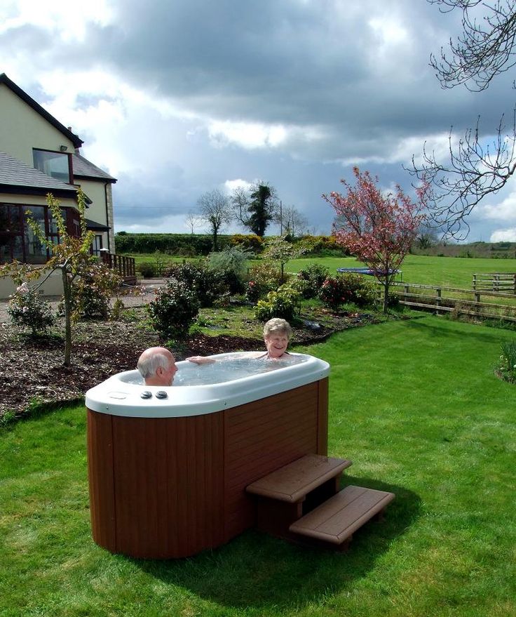 a large hot tub sitting in the middle of a lush green field next to a house