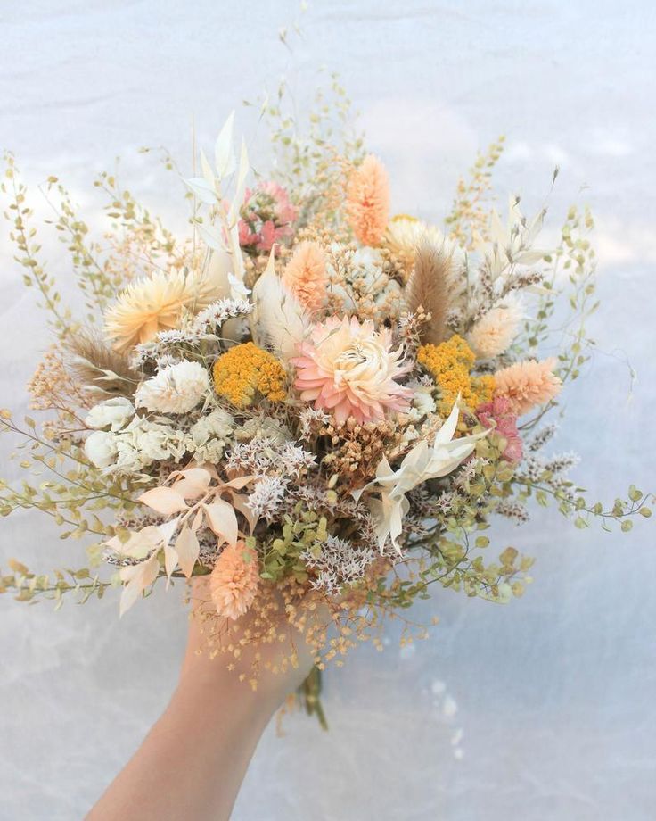 a person holding a bouquet of flowers in their hand with snow on the ground behind them