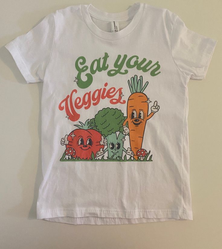 Our new Eat Your Veggies outfit is the outfit of spring! Snag a tee in Black or white, and even add a bottom! Available in adult tees as well! All styles of clothing will be the all over veggie print. Tees will have the graphic. Lounge tees and tanks are the all over print.  Sizing (Message Sizes): Graphic Tees: Babies+Toddlers(6/12M, 12/18M, 2T-5T), Kids (S-XL), and Adult (S-2X Unisex). Care:  To extend the wear of your item, it is recommended to use a gentle wash and tumble dry. If possible, hang-drying is always best for handmade items! Tees should be washed inside out and then hang dried.  Fabric Contents*: Double Brushed Polyester Material - 96% Polyester/4% Lycra Pullovers and Tees will be a thick DBP.  Graphic Tee is a Bella canvas tee.  Turn Around Time (TAT) and Shipping: Current Organic White Crew Neck Tops, Organic White Short Sleeve Tops, Organic White T-shirt For Summer, Organic White Crew Neck T-shirt, Organic White Graphic Print Tops, Fun White T-shirt, Funny White T-shirt For Spring, Spring Organic White T-shirt, Playful Summer T-shirt With Funny Text