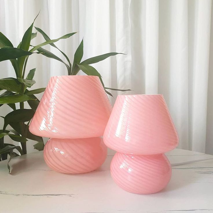 three pink vases sitting on top of a white table next to a potted plant