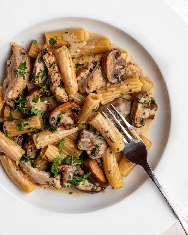 a white plate topped with pasta covered in mushrooms and parsley next to a fork