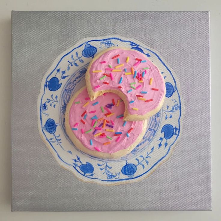 two donuts with pink frosting and sprinkles on a blue and white plate