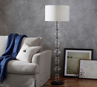 a living room with a couch, lamp and pictures on the floor next to it