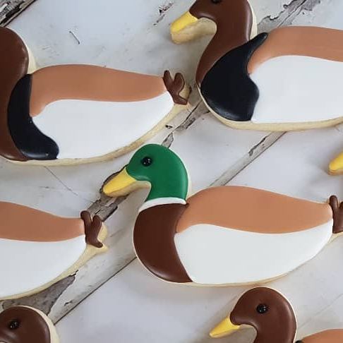 decorated cookies in the shape of ducks are arranged on a white table with wood planks