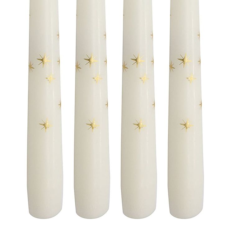 four white candles with gold stars on them are lined up against a white background,