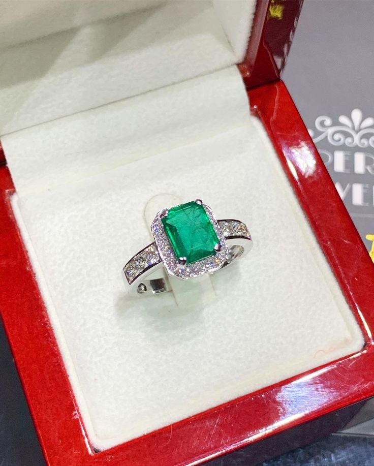 an emerald and diamond ring in a red box