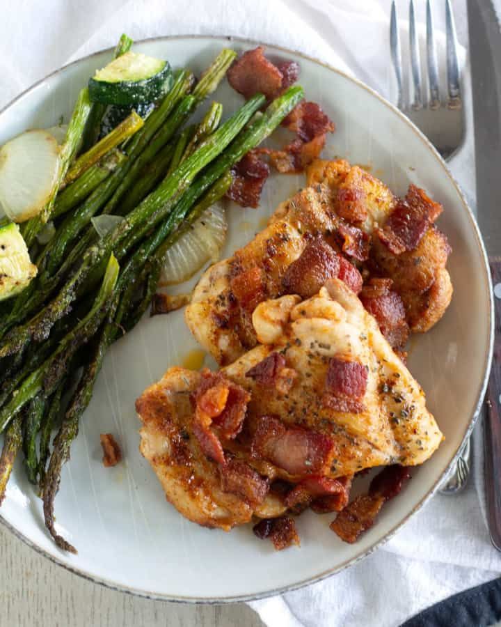 a white plate topped with chicken, asparagus and bacon next to a fork