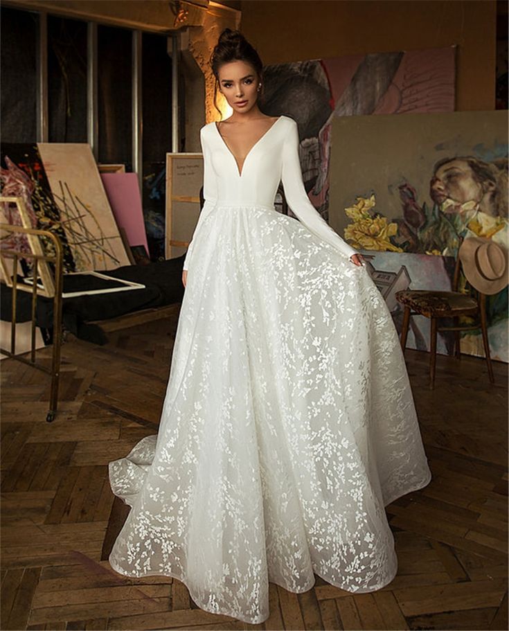 a woman in a white wedding dress standing on a wooden floor with paintings behind her