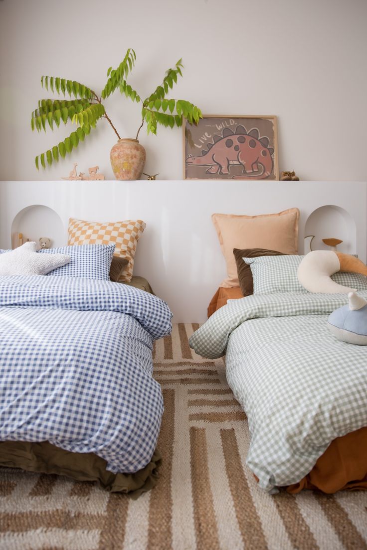 two beds with blue and white checkered covers in a room next to a potted plant