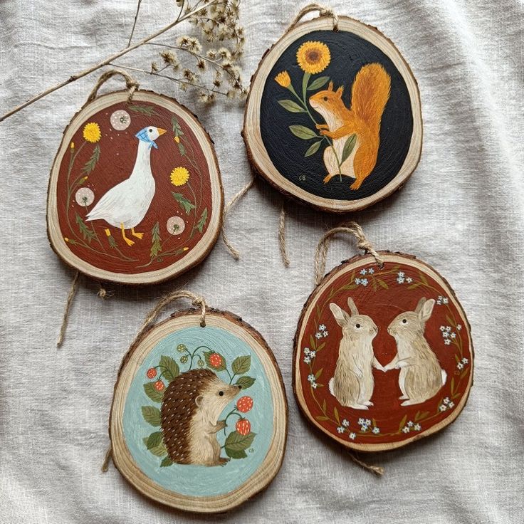 four hand painted wood slices with animals and flowers on them, hanging from twine