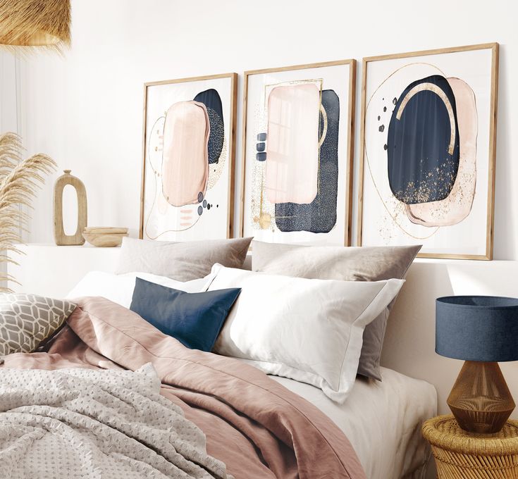 a bed with pink and gold pillows in a bedroom next to two pictures on the wall