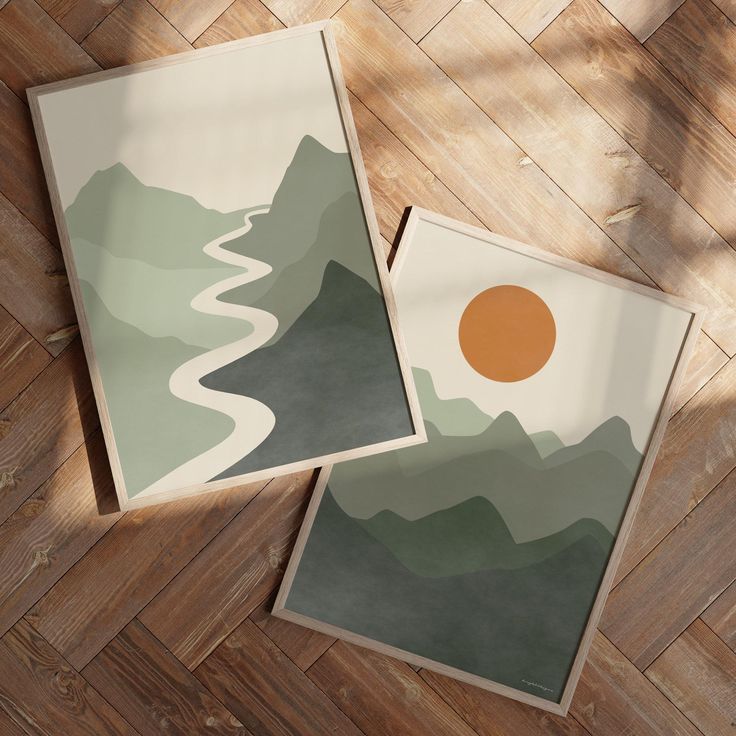 two framed pictures sitting on top of a wooden floor next to each other with mountains in the background