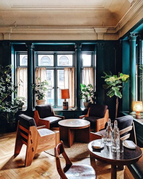 a living room filled with lots of furniture next to tall windows and potted plants