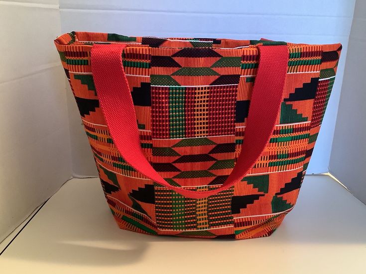 Kente fabric bucket tote bag.  Great for everyday, for shopping it can be used as a storage bag for bathroom items or cosmetics and for shopping.  Ships from Burlington, North Carolina.  The width across the top is 16 inches, the height is 11 inches and the depth on the side bottom in 4 inches.  African  cloth/fabric.  Great for a gift.  Great as a book bag or for a grocery bag, Casual Orange Shoulder Bucket Bag, Orange Large Capacity Tote Shoulder Bag, Large Capacity Orange Bag For Shopping, Large Capacity Orange Tote Shoulder Bag, Orange Bucket Bag For Daily Use, Orange Rectangular Bucket Bag For Shopping, Rectangular Orange Bucket Bag With Adjustable Strap, Casual Orange Tote Bucket Bag, Casual Orange Shopping Bag