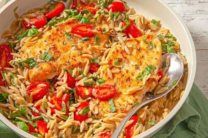 a white bowl filled with pasta and chicken covered in tomatoes, green onions and basil