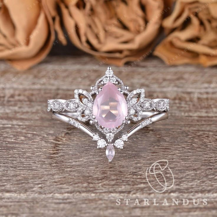 a pink diamond ring sitting on top of a wooden table next to some dried flowers