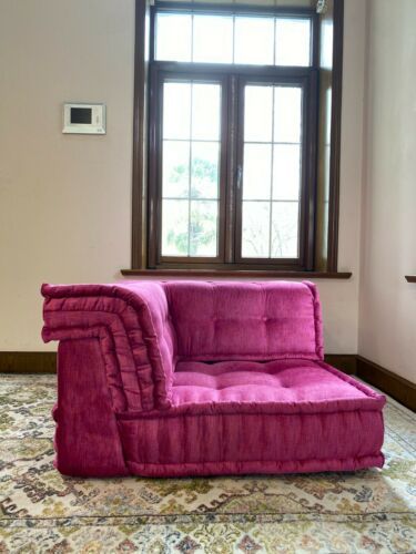 a pink couch sitting in front of a window on top of a carpeted floor