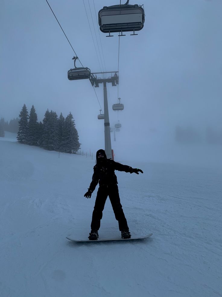 a person riding a snowboard on a snowy slope next to a ski chair lift