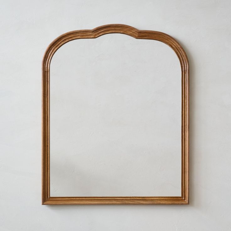 a wooden mirror hanging on the wall next to a white wall with a plant in it