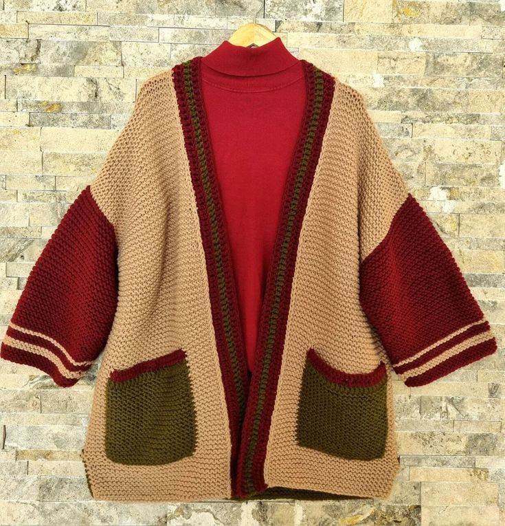 a cardigan sweater hanging on a brick wall next to a wooden hanger with a red shirt underneath it