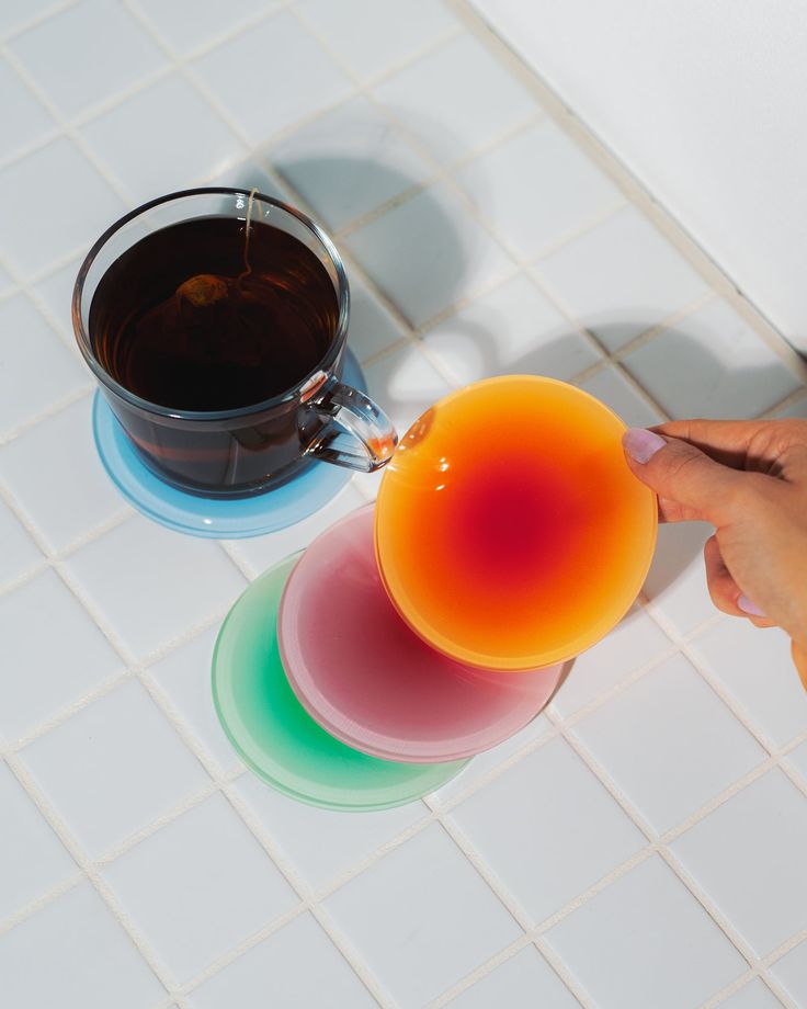 a person is pouring liquid from a cup into three different colored cups on a white tile floor