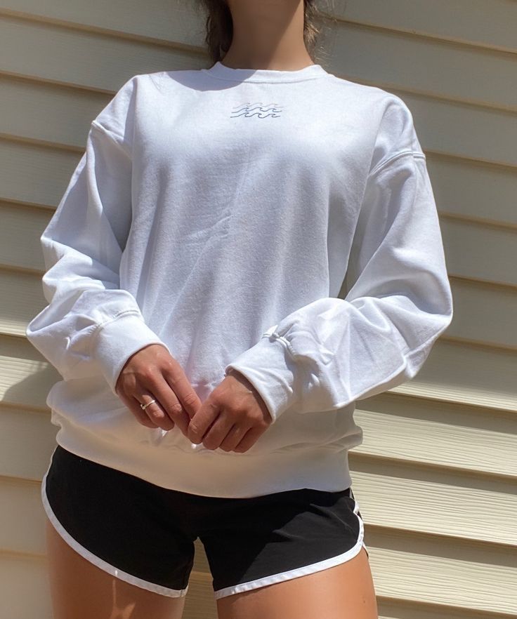 a woman in white shirt and black shorts standing next to a building with her hands on her hips