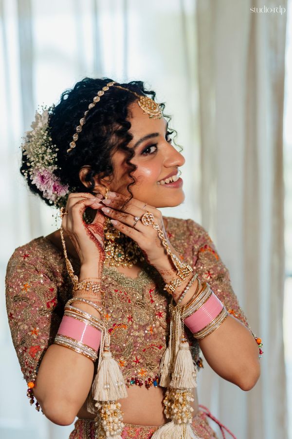 a woman in a bridal outfit smiles while holding her hands to her face and looking off into the distance